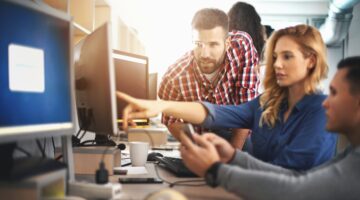 Drei junge Erwachsene arbeiten gemeinsam an einem Computerarbeitsplatz in einem modernen Büro, wobei