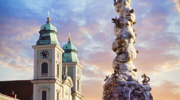 Die barocke Dreifaltigkeitssäule am Linzer Hauptplatz mit vergoldeter Sonnenkrone beim Sonnenunterga
