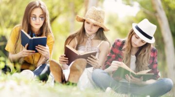 Drei junge Frauen sitzen im Sommer auf einer Wiese im Freien und lesen konzentriert je ein Buch, umg