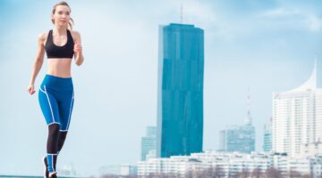 Eine junge Frau in blau-schwarzer Sportkleidung joggt im Freien mit der Wiener Skyline (DC Tower und