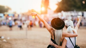 Zwei junge Frauen stehen von hinten fotografiert auf einem Musikfestival, halten ihre Getränkebecher