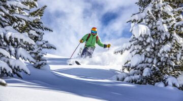 Ein Skifahrer in grüner Jacke und buntem Helm fährt dynamisch durch tief verschneiten Tiefschnee zwi