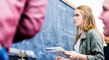 Eine junge Studentin mit langen roten Haaren steht konzentriert vor einer mit Formeln und Gleichunge