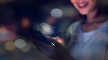 Eine lächelnde junge Frau hält ein Smartphone, aus dem ein leuchtend-holografischer Fingerabdruck mi