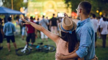 Ein junges Pärchen steht eng umschlungen auf einem Outdoor-Festival und blickt gemeinsam in Richtung