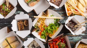 Vogelperspektive auf zahlreiche weiße Takeaway-Boxen mit verschiedenen asiatischen Gerichten wie Frü