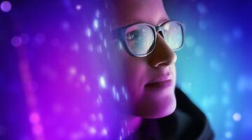 Eine junge Frau mit Brille wird von violett-blauem Bokeh-Licht angestrahlt, das sich in ihren Gläser
