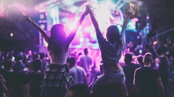 Zwei junge Frauen feiern ausgelassen auf einem Open-Air-Konzert oder Musikfestival, ihre Arme in die