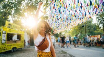 Eine junge Frau tanzt ausgelassen auf einem Outdoor-Festival, umgeben von bunten Papierfähnchen und 