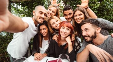 Eine fröhliche Gruppe von sieben jungen Erwachsenen macht ein Selfie bei einem gemeinsamen Abendesse