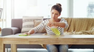 Eine junge Frau im Streifenpullover putzt konzentriert einen Holzcouchtisch im Wohnzimmer, mit einem