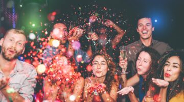 Eine ausgelassene Gruppe junger Menschen feiert auf einer Party und bläst buntes Konfetti in die Luf