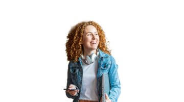 Eine lachende junge Frau mit lockigem roten Haar trägt einen Laptop unter dem Arm, hält ein Smartpho