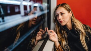 Eine junge Frau sitzt in einem Zug oder einer U-Bahn und schaut nachdenklich aus dem Fenster, ihre S