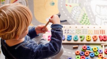 Ein Kleinkind spielt konzentriert mit einem bunten Holz-Lernspielzeug mit Zahlen von 1 bis 10 und bu