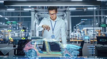 Ein Ingenieur mit Brille und Namensschild interagiert in einer modernen Automobilfabrik mit einem ho