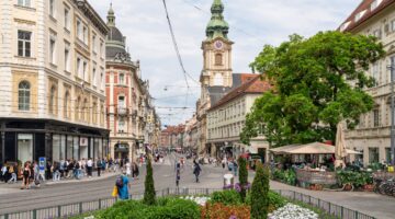 Belebte Fußgängerzone in Graz mit historischen Gründerzeitgebäuden, dem Kirchturm der Stadtpfarrkirc
