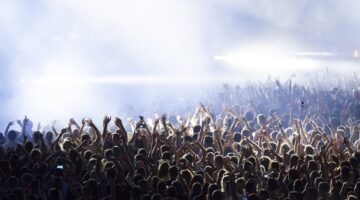 Eine riesige Menschenmenge bei einem Konzert oder Festival reckt die Arme in die Luft, während drama