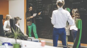 Ein junger Mann präsentiert vor einer großen Kreidetafel mit technischen Diagrammen (App-Architektur