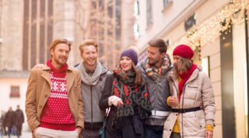 Fünf fröhliche junge Erwachsene in Winterkleidung spazieren lachend durch eine winterliche Wiener In
