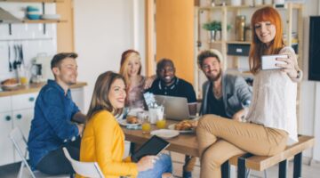 Eine Gruppe von sechs jungen, diversen Menschen versammelt sich in einer modernen WG-Küche beim geme