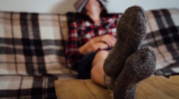 Eine Person liegt entspannt auf einem karierten Sofa mit einem Buch über dem Gesicht, während ihre m