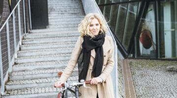 Eine junge blonde Frau mit lockigem Haar steht mit einem schwarzen Fixie-Fahrrad mit roten Felgen au