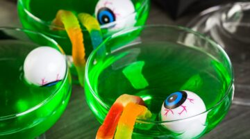 Zwei grüne Halloween-Cocktails in Martini-Gläsern, dekoriert mit Gummiwürmern und Plastik-Augen als