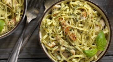 Zwei Schüsseln mit Tagliatelle in Pesto-Sauce mit gegrillten Hähnchenstreifen und frischem Basilikum