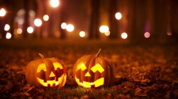 Zwei leuchtende Halloween-Kürbisse (Jack-o'-Lanterns) mit geschnitzten Gesichtern stehen auf herbstl