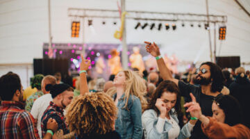 Eine ausgelassene Menschenmenge tanzt vor einer beleuchteten Bühne in einem Festivalzelt, mit grünen