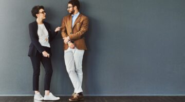 Eine junge Frau und ein junger Mann in smarter Business-Casual-Kleidung stehen vor einer grauen Wand