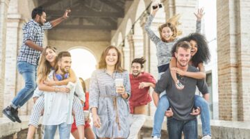 Eine fröhliche, diverse Gruppe von etwa acht jungen Menschen posiert ausgelassen vor einem historisc