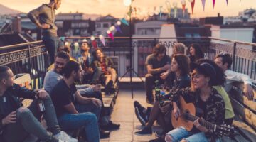 Eine lebhafte Gruppe junger Menschen feiert eine Rooftop-Party bei Sonnenuntergang, mit Lichterkette