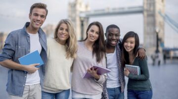 Multikulturelle Studierendengruppe (5 junge Erwachsene) mit Notizbloecken vor der Tower Bridge in Lo