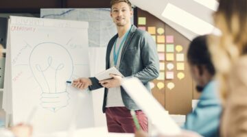 Junger Mann präsentiert kreative Startup-Ideen an einem Whiteboard mit Glühbirnen-Zeichnung und Begr